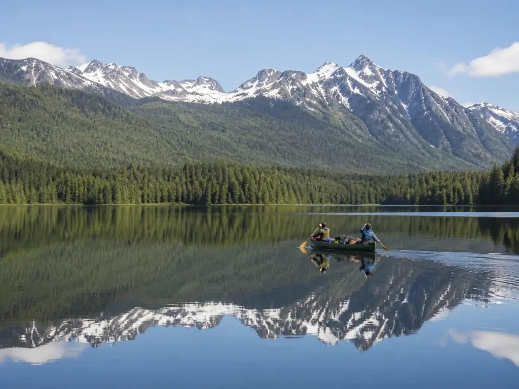 A canoe crossing calm water beneath the snow-streaked peaks of the western Cariboo Range
