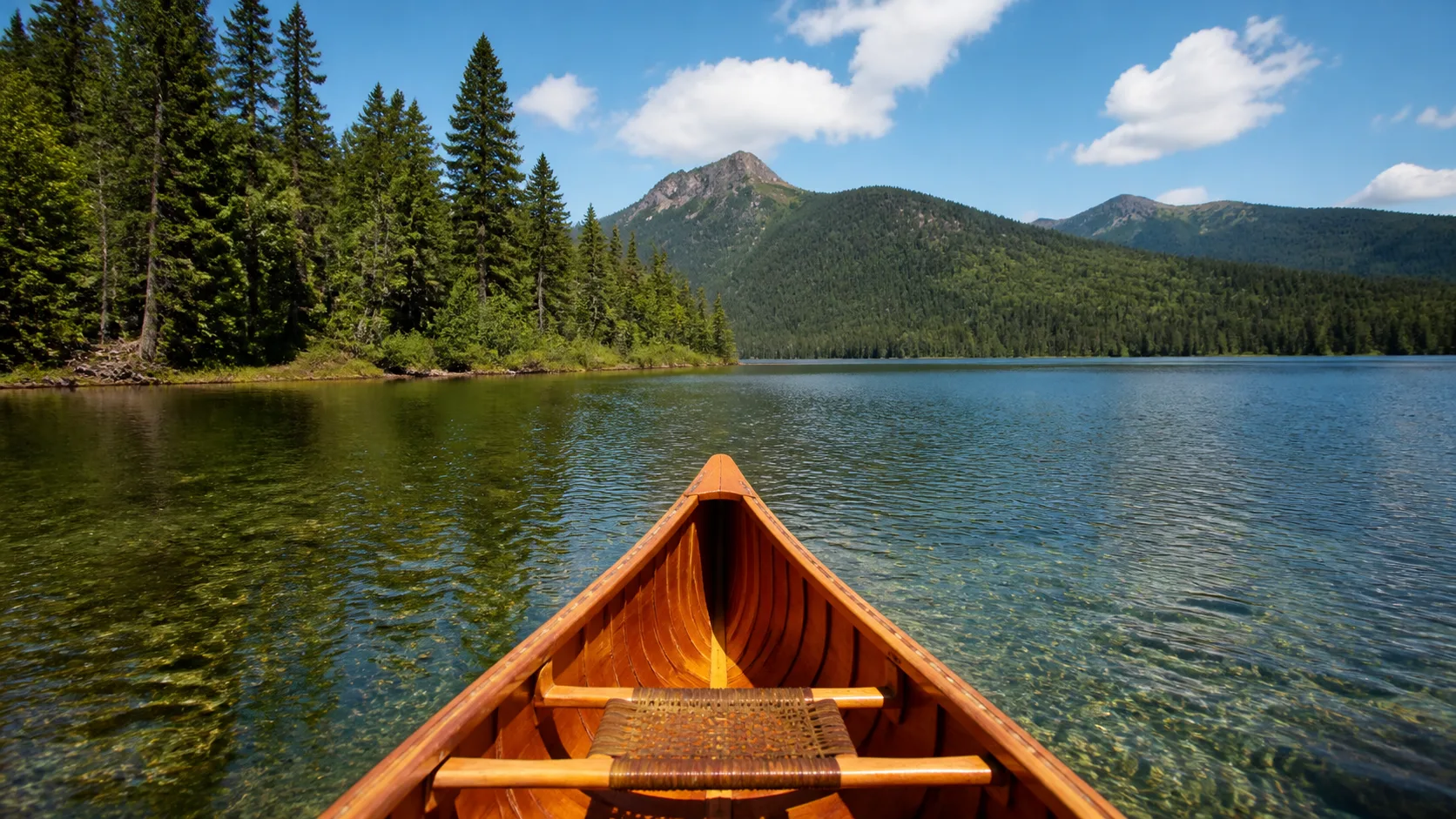 Bow of a rental canoe gliding across clear water on the Bowron Lake Circuit