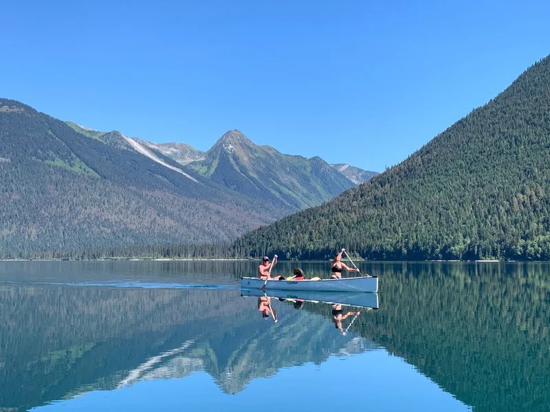 A canoe on turquoise water below the snow-streaked Cariboo peaks