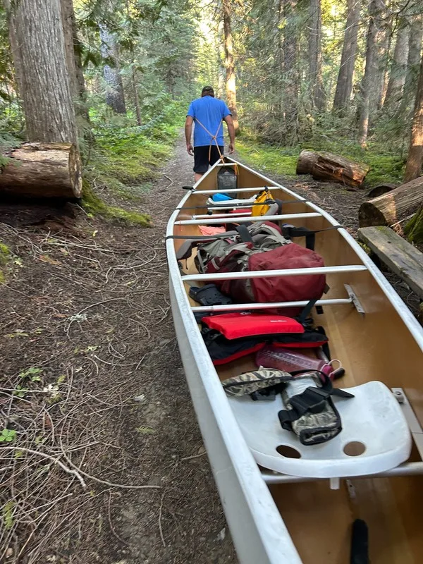 A loaded canoe resting on the portage trail beside the forest