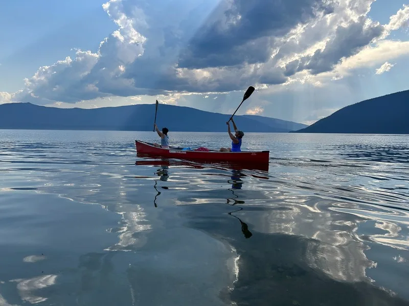 Two paddlers in a red canoe raising their paddles on open water under a dramatic sky