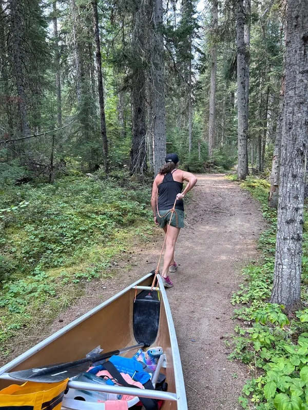 A paddler towing a loaded canoe on a cart along a forest portage trail at Bowron Lake