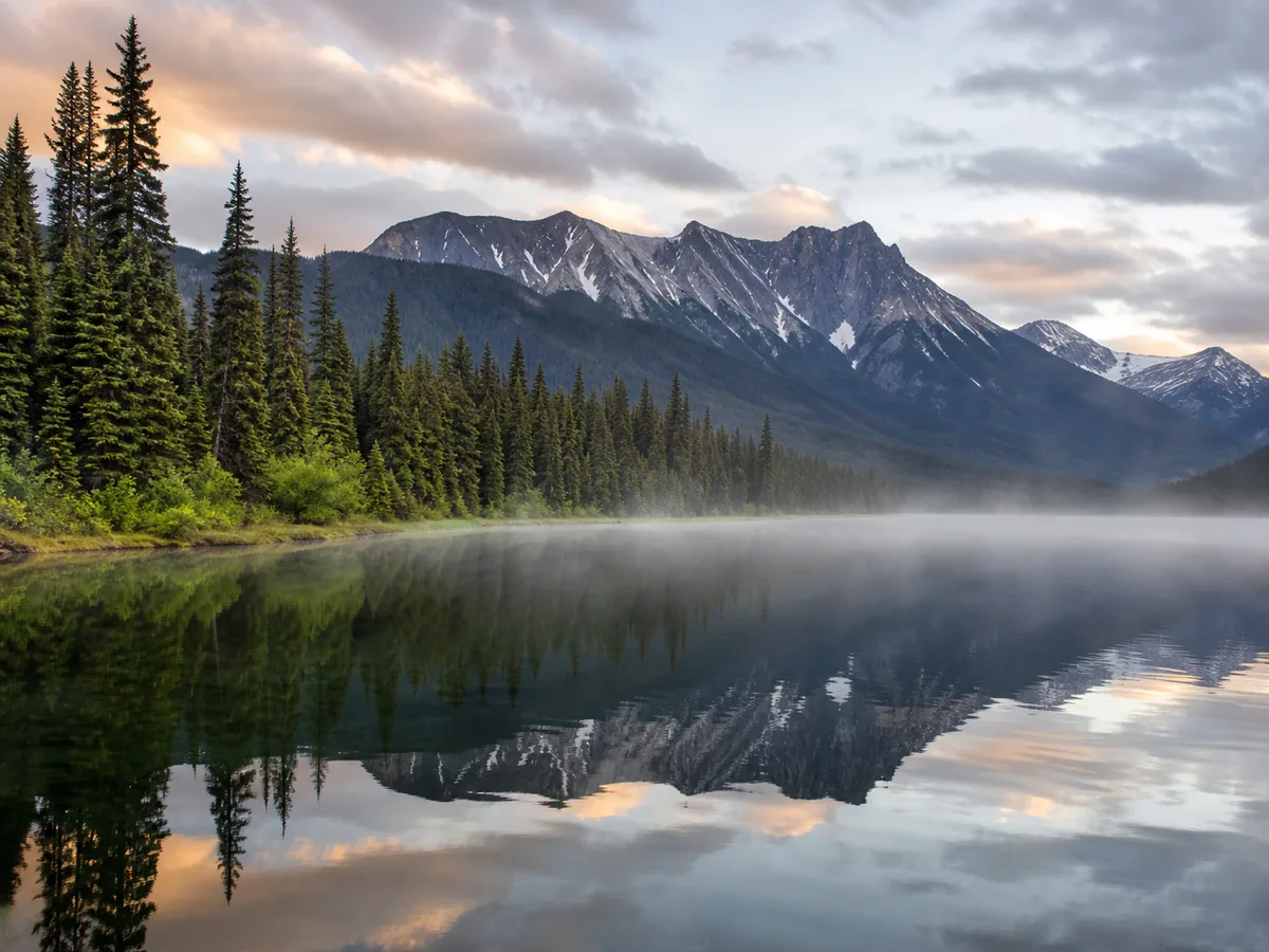 Mist lifting off still water at dawn on Bowron Lake